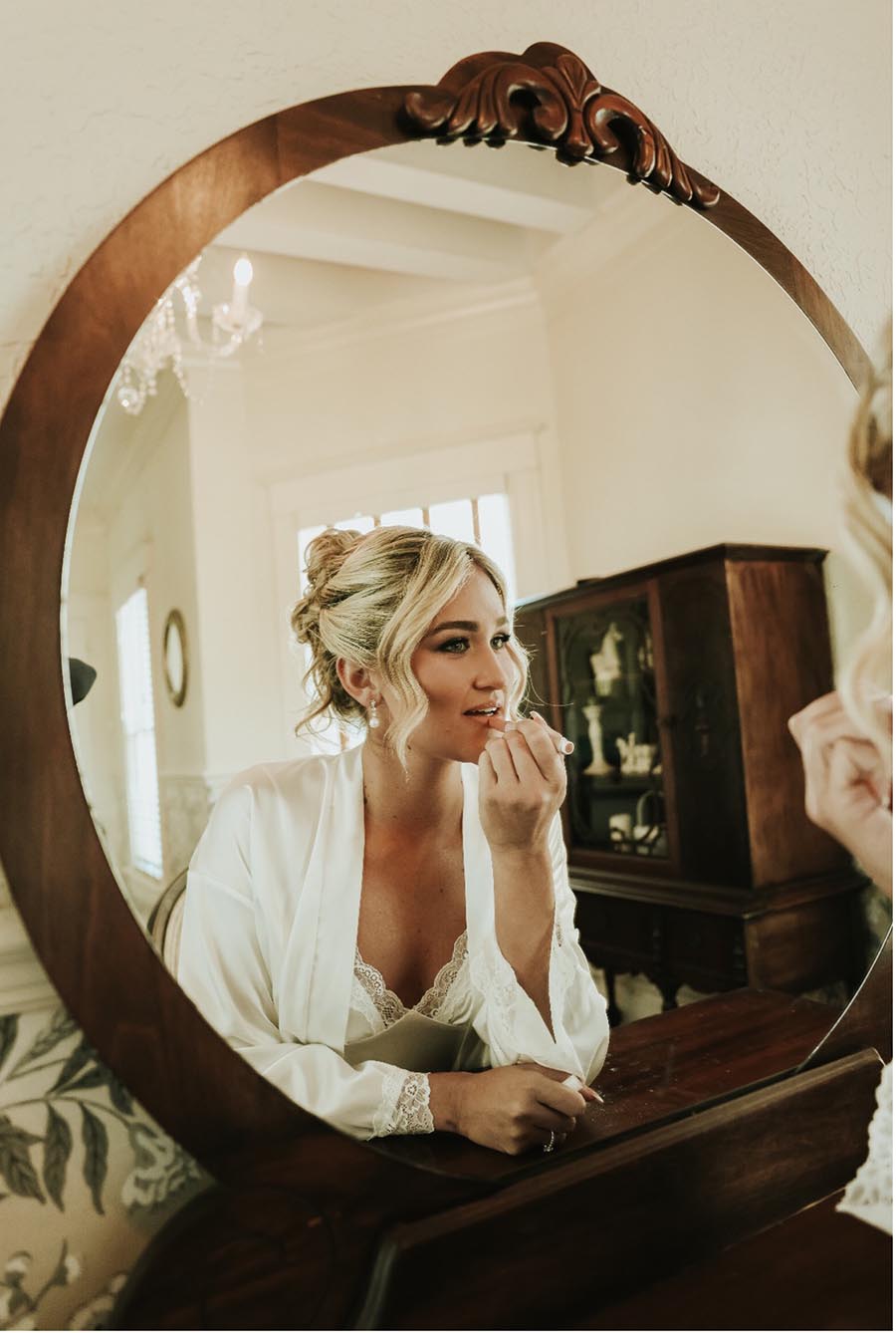 bride applying lipstick while looking into her reflection in the mirror