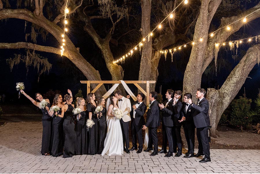 entire wedding party cheering the bride and groom as they kiss under the oak tree