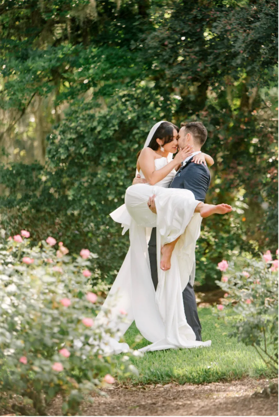 Groom holding bride in his arms while standing in rose garden