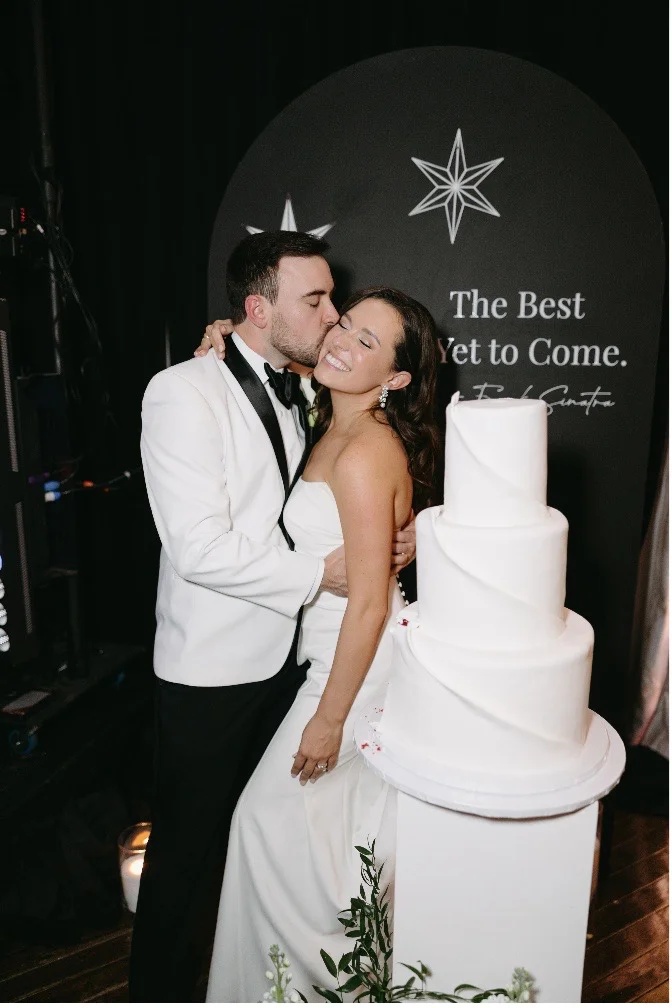 groom kissing the bride next to their wedding cake at The Highland Manor, Ashley Lotus Photography