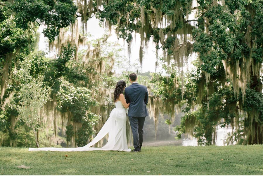 wedding-couple-standing-on-edge-of-a-lake-surrounded-by-trees